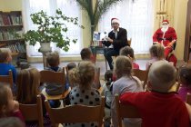 Pan Patryk w czapce Mikołaja pokazuje dzieciom czytaną książkę